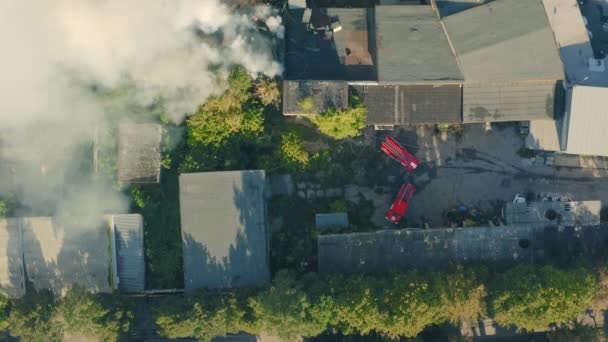 Een brand blussen in een pakhuis door een brandweer. Rook uit het vuur stijgt boven de daken. — Stockvideo