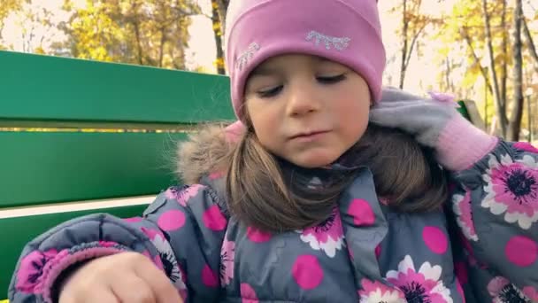 Negligenciado pequena menina com fome 4 anos de idade em um chapéu rosa e casaco quente comendo marshmallows ao ar livre — Vídeo de Stock