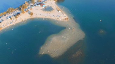 Many people swim in the water of the blue lake near the sandy yellow beach - top view aerial view