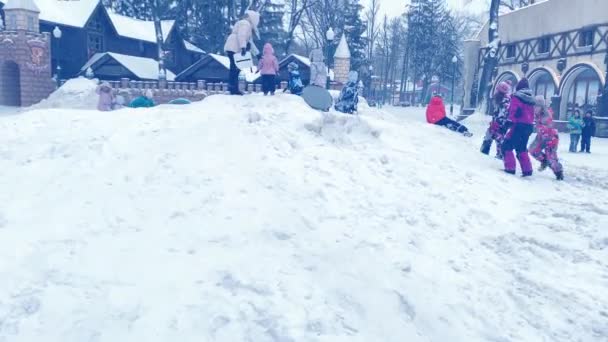 As crianças brincam alegremente fora no escorrega de neve no parque no inverno durante a queda de neve — Vídeo de Stock
