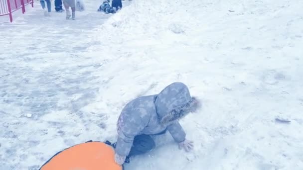 Милая девочка взбирается на снежную горку со снежным ковриком в руке. — стоковое видео