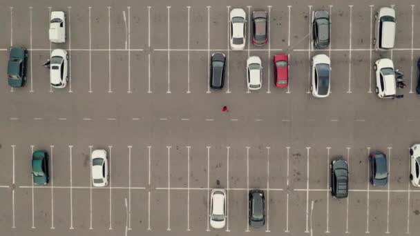 Άνδρας με κόκκινα ρούχα περπατά μέσα από ένα χώρο στάθμευσης αυτοκινήτων μεταξύ των αυτοκινήτων - γενικά πυροβόλησε — Αρχείο Βίντεο