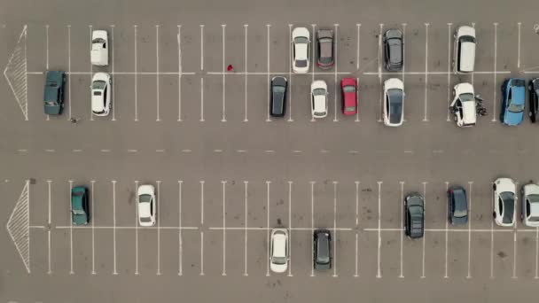 Hombre con chaqueta roja cruza la carretera en un aparcamiento: vista superior zoom en tiro. Conductor camina a su coche. — Vídeos de Stock