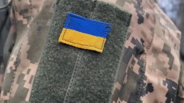 Kamuflajlı bir askerin omzunda Ukrayna bayrağı. Ukrayna 'nın sembolü, Ukrayna ordusunun silahlı bir askerinin sembolü olan mavi-sarı bayrak..