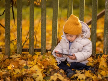 Tarz sahibi çocuk dışarıda, yaprakların arasında oturmuş elinde akıllı bir telefonla çizgi film seyrediyor. Bir kız internette farklı oyunlar oynayıp eğlenmek için modern bir alet kullanıyor..