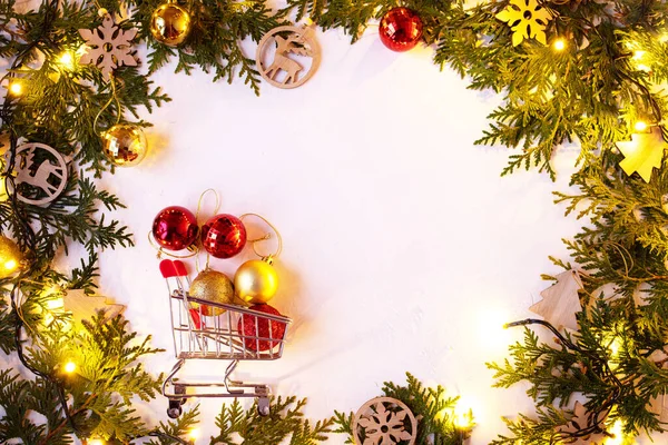 Noel ya da Yeni Yıl arkaplanı: Ahşap oyuncaklar ve parlak bir çelenk, çanlar, toplar ile beyaz arka planda köknar dalları. Tebrik için beyaz çerçeve. Noel toplarıyla alışveriş sepeti.