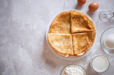 İki çiğ kahverengi yumurta, un, süt, şeker ve çırpı hamurlu krep malzemesi olarak mermer gri amd beyaz yüzey.