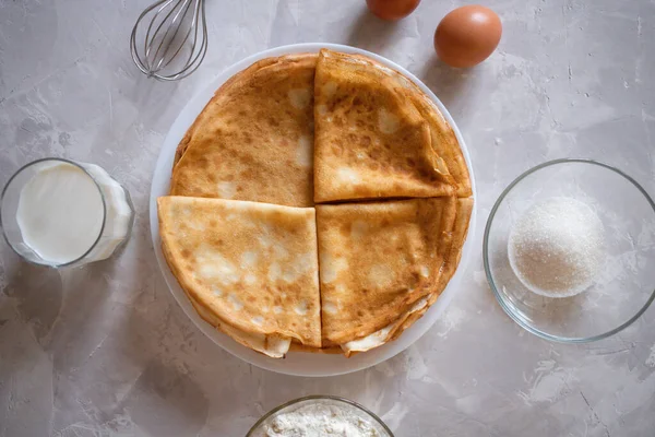 İki çiğ kahverengi yumurta, un, süt, şeker ve çırpı hamurlu krep malzemesi olarak mermer gri amd beyaz yüzey.