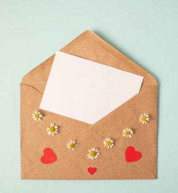 Sevgililer günü için tebrik kartı konsepti, düğün ya da anneler günü, kadınlar günü. İçinde boş kağıt ve güzel kırmızı kağıt kalpler olan bir zarf aç. Mavi papatya, nane arkaplan.