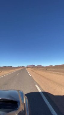 Çölde at sürerken, araba kumlu yolda, ufuk çizgisinde gidiyor. 