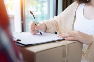 Kırmızı üniformalı teslimatçı paketini kapatırken, müşteri kadın belgeleri alırken imza atıyor..