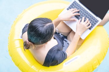 Tatilde çalışan serbest çalışan kadınlar havuzda lastik halkanın üzerinde otururken dizüstü bilgisayarda yazan genç bir kadın. Her yerden çalış, serbest çalış..