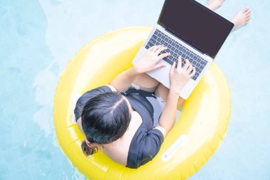 Tatilde çalışan serbest çalışan kadınlar havuzda lastik halkanın üzerinde otururken dizüstü bilgisayarda yazan genç bir kadın. Her yerden çalış, serbest çalış..