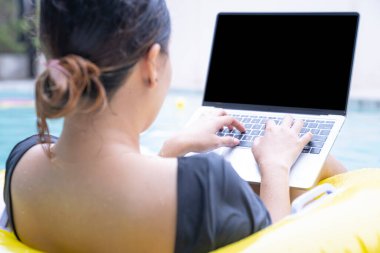 Tatilde çalışan serbest çalışan kadınlar havuzda lastik halkanın üzerinde otururken dizüstü bilgisayarda yazan genç bir kadın. Her yerden çalış, serbest çalış..