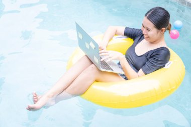 Tatilde çalışan serbest çalışan kadınlar havuzda lastik halkanın üzerinde otururken dizüstü bilgisayarda yazan genç bir kadın. Her yerden çalış, serbest çalış..