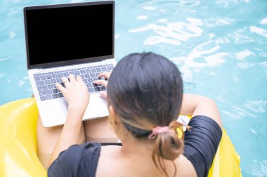 Tatilde çalışan serbest çalışan kadınlar havuzda lastik halkanın üzerinde otururken dizüstü bilgisayarda yazan genç bir kadın. Her yerden çalış, serbest çalış..