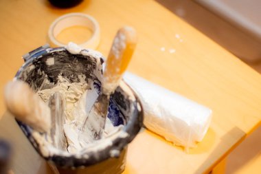 Ressamın mesleğinin ayrıntıları içinde macun bulunan siyah bir kap, iki spatula ve masanın üzerinde mobilya ve krep bandını kaplamak için plastik bir kap içerir..
