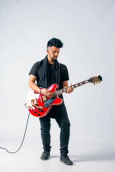 stock image Studio shot of a brown-skinned Latino man with dark hair and beard dressed in black clothing playing a red electric guitar on a white background.