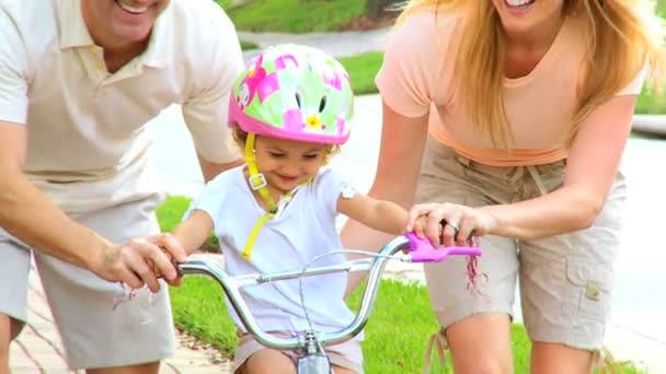 Jovens pais apoiando a criança na bicicleta pequena — Vídeo de Stock