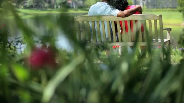 Amor pareja étnica planificación futuro al aire libre en el banco — Vídeos de Stock