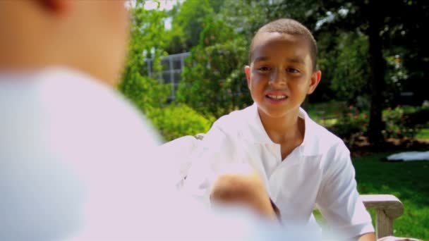 Kleine ethnische Jungen sitzen auf Gartenbank — Stockvideo