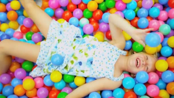 Смеющаяся маленькая девочка играет в пластиковые шарики — стоковое видео