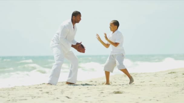 Ethnic father and son playing together American football on beach — Stock Video