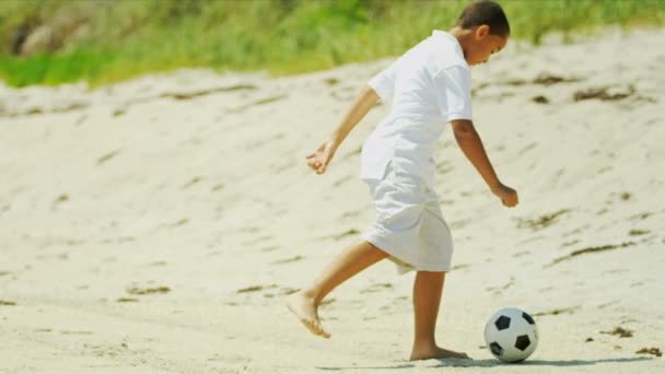 Этнический мальчик пинает футбольный мяч на пляже — стоковое видео