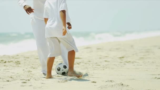 Ethnic parent teaching son playing football on beach — Stock Video