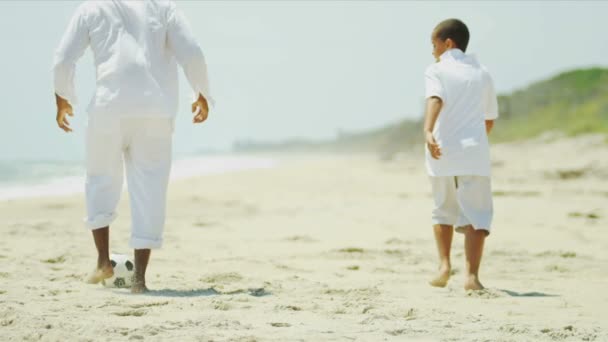 Этнические родители учат сына играть в футбол на пляже — стоковое видео