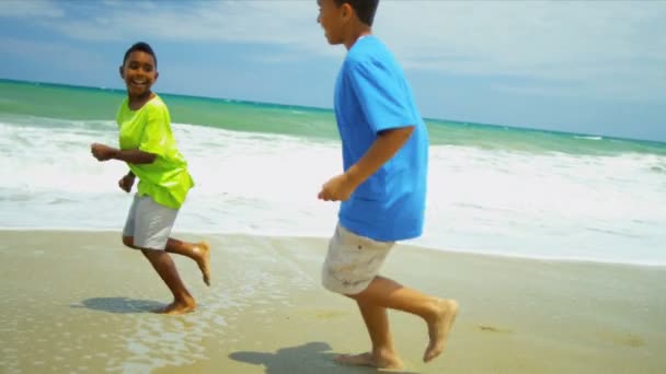 Этнические улыбающиеся мальчики бегут вместе по пляжу — стоковое видео
