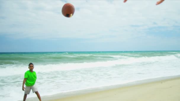Разнообразные мальчики практикуют вместе американский футбол на отдыхе у океана — стоковое видео