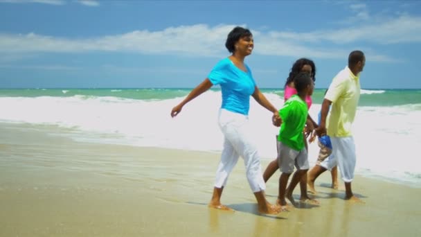 Padres afroamericanos caminando y relajándose con niños tomados de la mano en la playa — Vídeos de Stock