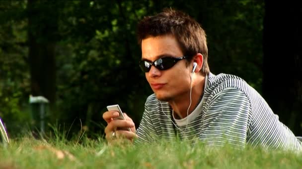 Молодой мужчина лежит в парке и слушает музыку. — стоковое видео