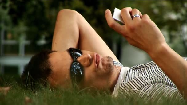 Young male lying in the park listening to music — Stock Video