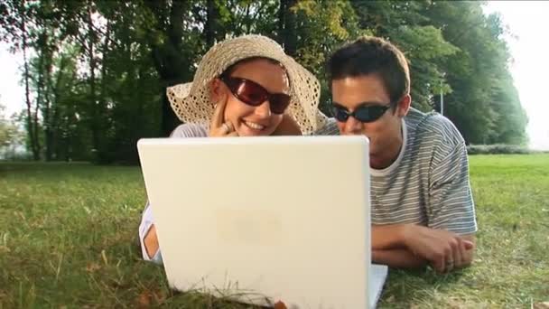 Casal jovem usando laptop em um parque em um dia de verão — Vídeo de Stock