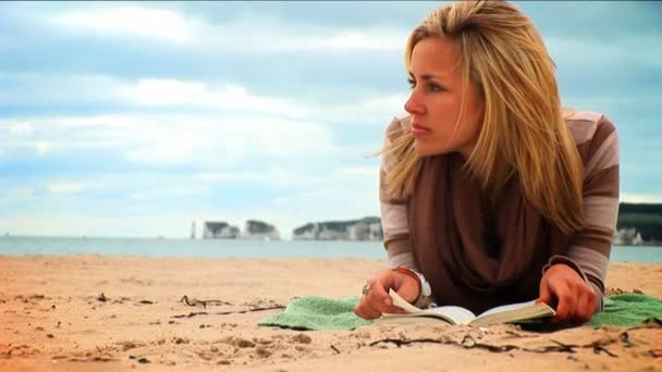 Mooie jonge blonde meisje lezen op het strand — Stockvideo