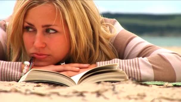 年轻美丽的金发女孩在沙滩上阅读 — 图库视频影像
