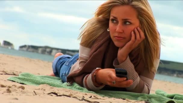 Blonde Mädchen SMS-Nachrichten am Strand — Stockvideo