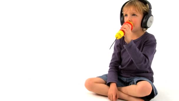 Μικρό ξανθό αγόρι, φορώντας ακουστικά & τραγούδι στο παιχνίδι μικρόφωνο — Αρχείο Βίντεο