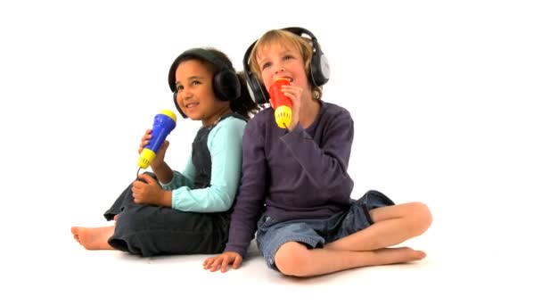 Little african american girl & blonde boy wearing earphones & singing into toy microphone — Stock Video