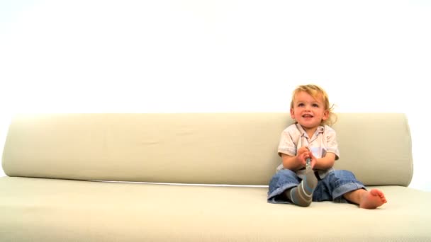 Lindo niño caucásico jugando en un sofá y quitándose los calcetines — Vídeos de Stock