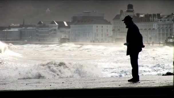 Пляжный пешеход храбро преодолевает волны прибрежной бури — стоковое видео