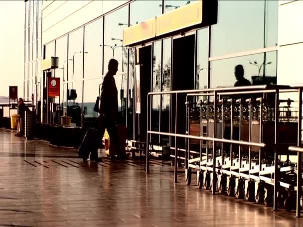 Airline passengers passing into airport terminal in silhouette — Stock Video