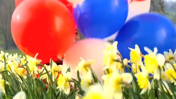 Cute african american child playing with balloons in a field of daffodils — Stock Video