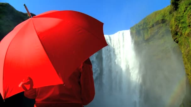 Begreppet skott av ensamstående kvinna vid ett vattenfall med rött paraply — Stockvideo