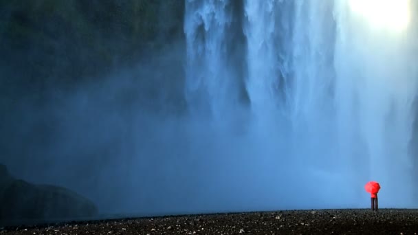 Concept shot of lone female on the edge of a waterfall with red umbrella — Stock Video