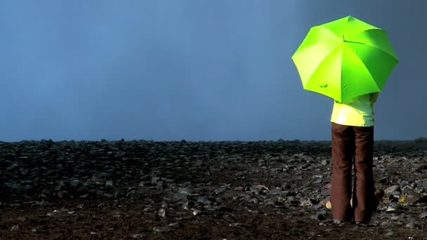 Conceito tiro de fêmea solitária em pé na borda de uma cachoeira com guarda-chuva verde — Vídeo de Stock