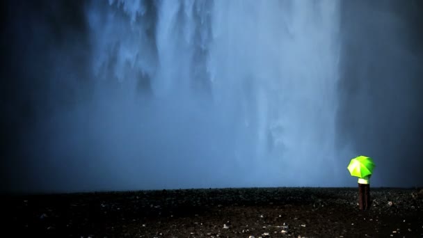 Begreppet skott av ensamstående kvinna står på kanten av ett vattenfall med grönt paraply — Stockvideo