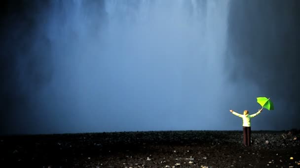 Conceito tiro de fêmea solitária em pé na borda de uma cachoeira com guarda-chuva verde — Vídeo de Stock